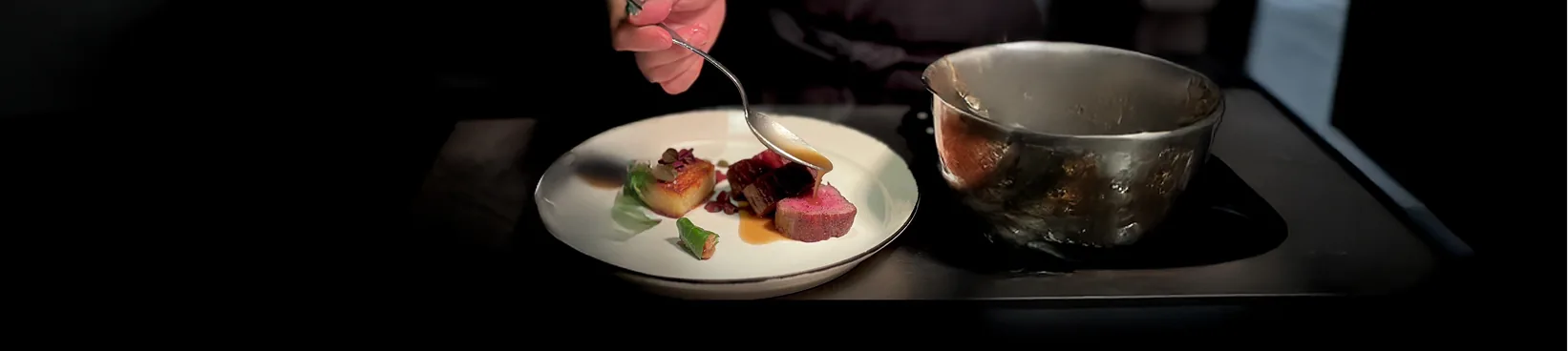 Le chef nappe de sauce une viande rosée à l'assiette