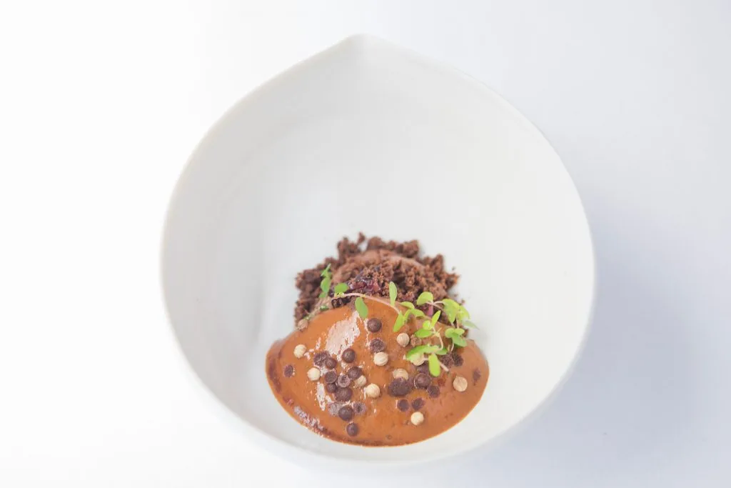 Assiette creuse : sauce brune, crumble sombre, épices et jeunes pousses