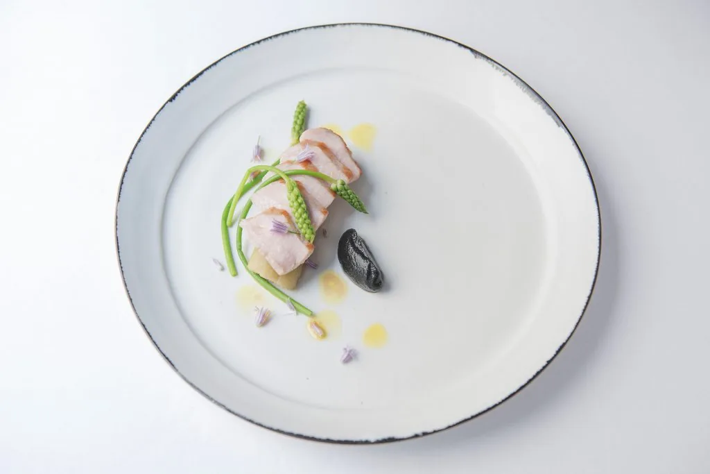 Fines tranches de viande rosée, asperges vertes, fleurs mauves et quenelle noire
