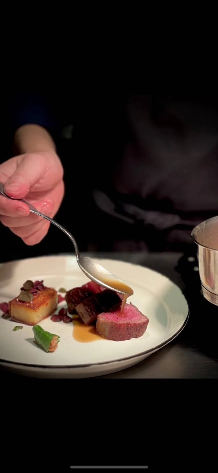 Le chef nappe de sauce une viande rosée à l'assiette