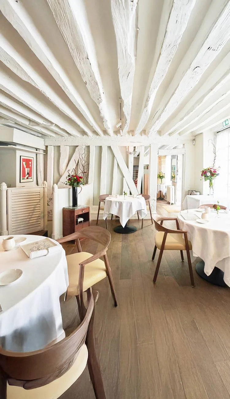 Salle du restaurant : tables nappées de blanc sous les poutres apparentes